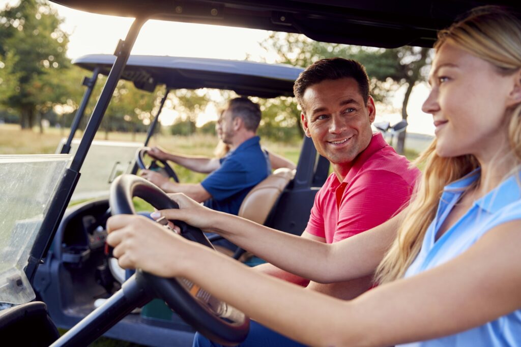 Mature And Mid Adult Couples Driving Buggies Playing Round On Golf Together